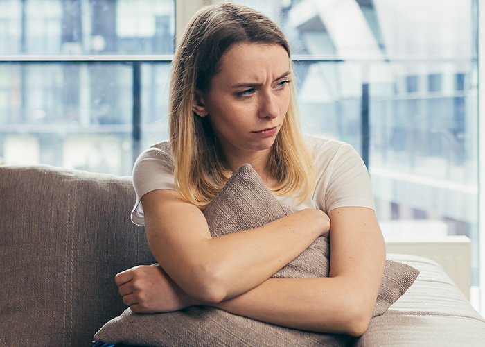 Frustrated woman sitting indoors hugging a pillow, reflecting the stress of a mom taking kids on a 9-hour flight. Frustrated woman sitting indoors hugging a pillow, reflecting the stress of a mom taking kids on a 9-hour flight.