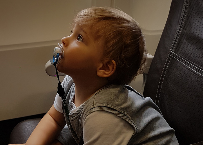 Young child with pacifier sitting on airplane seat, highlighting challenges of long flights with kids. Young child with pacifier sitting on airplane seat, highlighting challenges of long flights with kids.