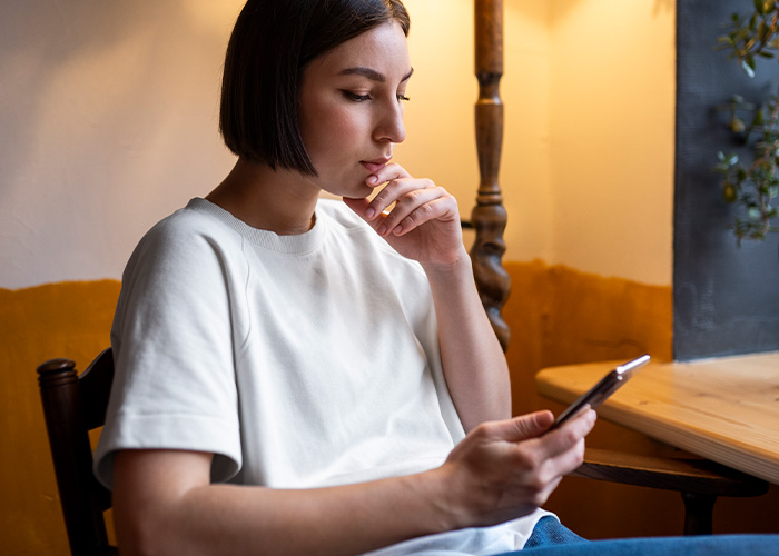 Woman in white shirt thoughtfully looking at phone, facing dilemma over savings after parents claim financial rights. Woman in white shirt thoughtfully looking at phone, facing dilemma over savings after parents claim financial rights.