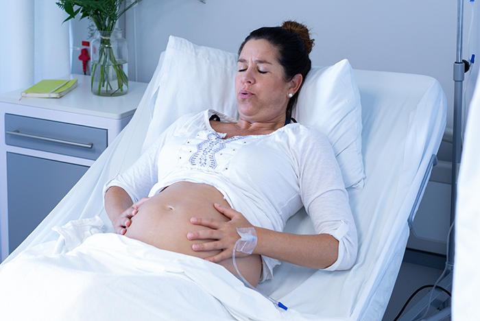 Woman in hospital bed holding her pregnant belly, recovering after scheduled C-section with IV drip attached. Woman in hospital bed holding her pregnant belly, recovering after scheduled C-section with IV drip attached.