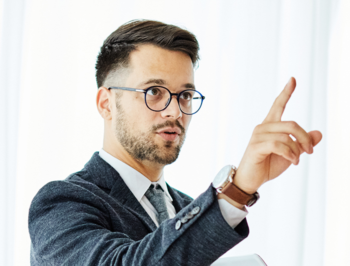 Manager wearing glasses and suit pointing finger while discussing work performance in a bright office setting Manager wearing glasses and suit pointing finger while discussing work performance in a bright office setting