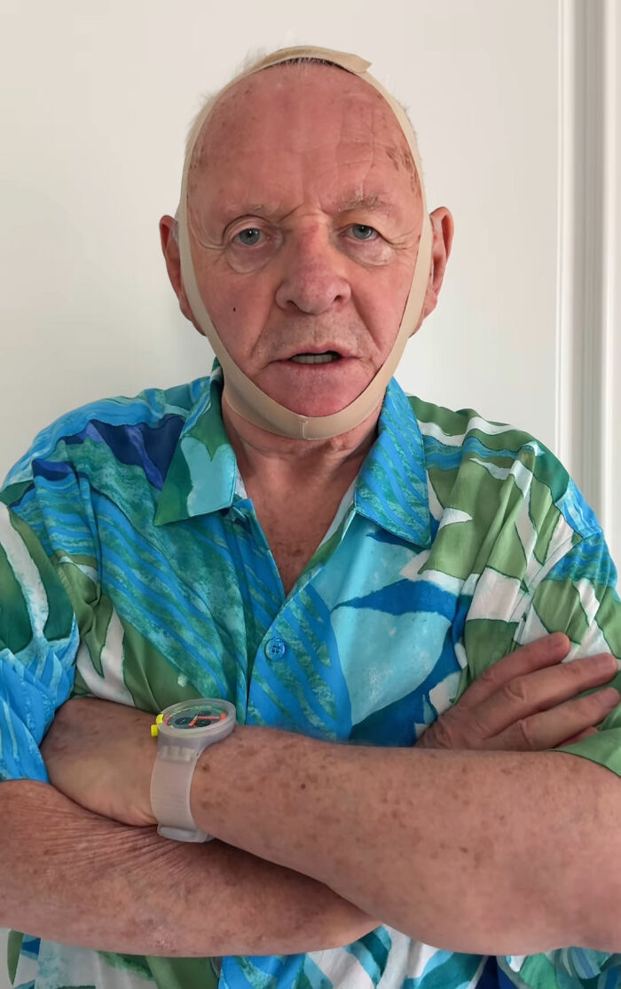 Anthony Hopkins wearing a face strap, parodying a viral beauty product in a colorful shirt with arms crossed. Anthony Hopkins wearing a face strap, parodying a viral beauty product in a colorful shirt with arms crossed.