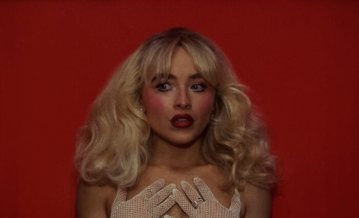 Blonde woman with dramatic makeup and fishnet gloves poses against a red background, evoking a sensual pole dance vibe. Blonde woman with dramatic makeup and fishnet gloves poses against a red background, evoking a sensual pole dance vibe.