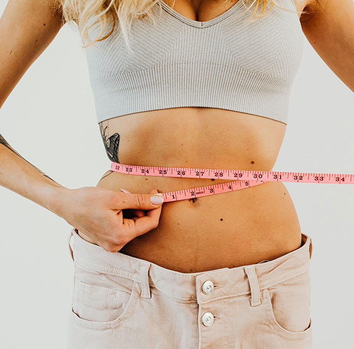 Woman measuring waist with pink tape measure, symbolizing weight loss related to Ozempic vulva side effects. Woman measuring waist with pink tape measure, symbolizing weight loss related to Ozempic vulva side effects.