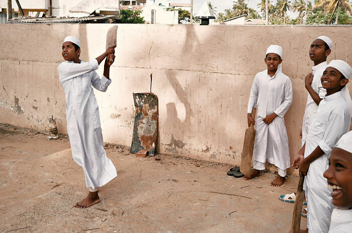 Boys in traditional clothing playing cricket outdoors in Asia, capturing candid everyday moments by photographer Gil Kreslavsky.