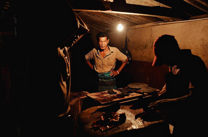 Asian men working in a dimly lit room, capturing candid everyday moments from Asia by photographer Gil Kreslavsky.