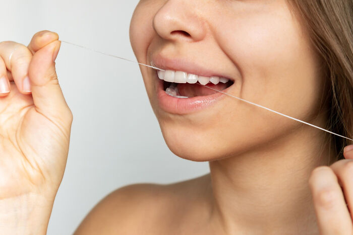 Close-up of a woman flossing her teeth demonstrating a low effort, high reward oral hygiene routine for better health.