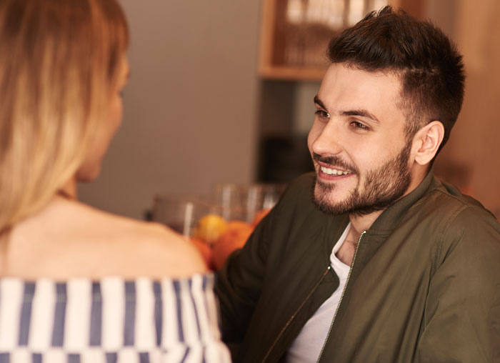 Man smiling and talking to woman in a casual setting illustrating man tells wife she couldn’t do it without him concept.