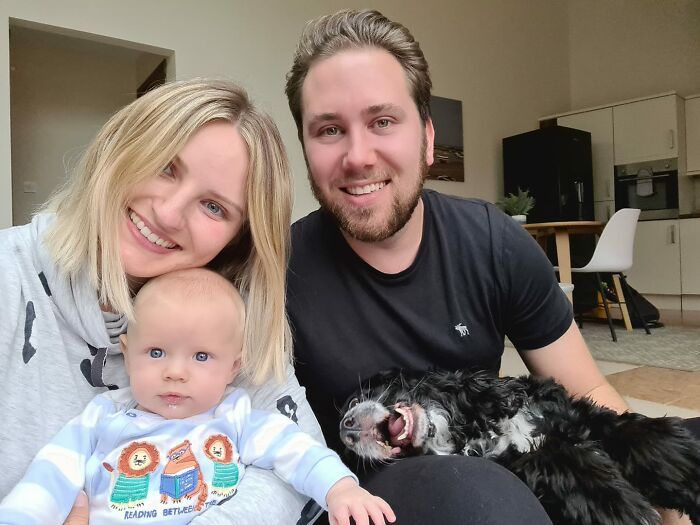 Happy family with a baby and a dog playfully crashing the photo in a cozy home setting, showcasing funny times pets.