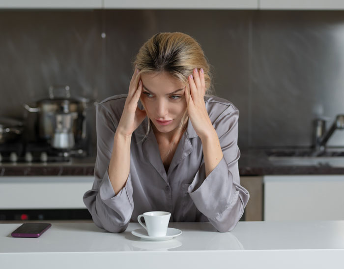 Woman in pajamas sitting at kitchen counter looking stressed, illustrating determination to prove husband wrong.