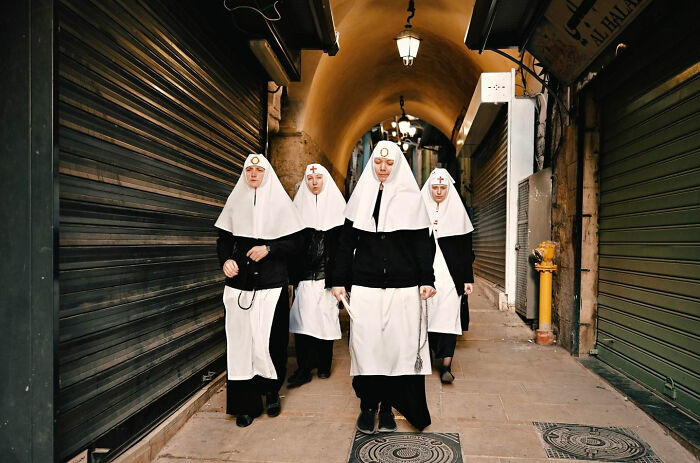Four women dressed as nuns walking through a dimly lit alleyway, highlighting candid everyday moments from Asia.
