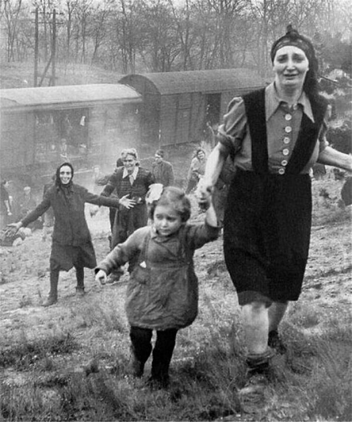 Black and white historical photo showing a group of people, including a woman and child, walking uphill near a train carriage.