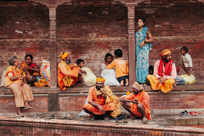 Group of people in traditional attire sharing candid everyday moments in Asia near a brick structure with pillars.