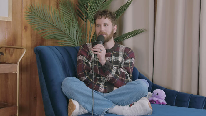 Man sitting on a blue couch holding a microphone, surrounded by plants, illustrating celebrities Hollywood tried to make stars.