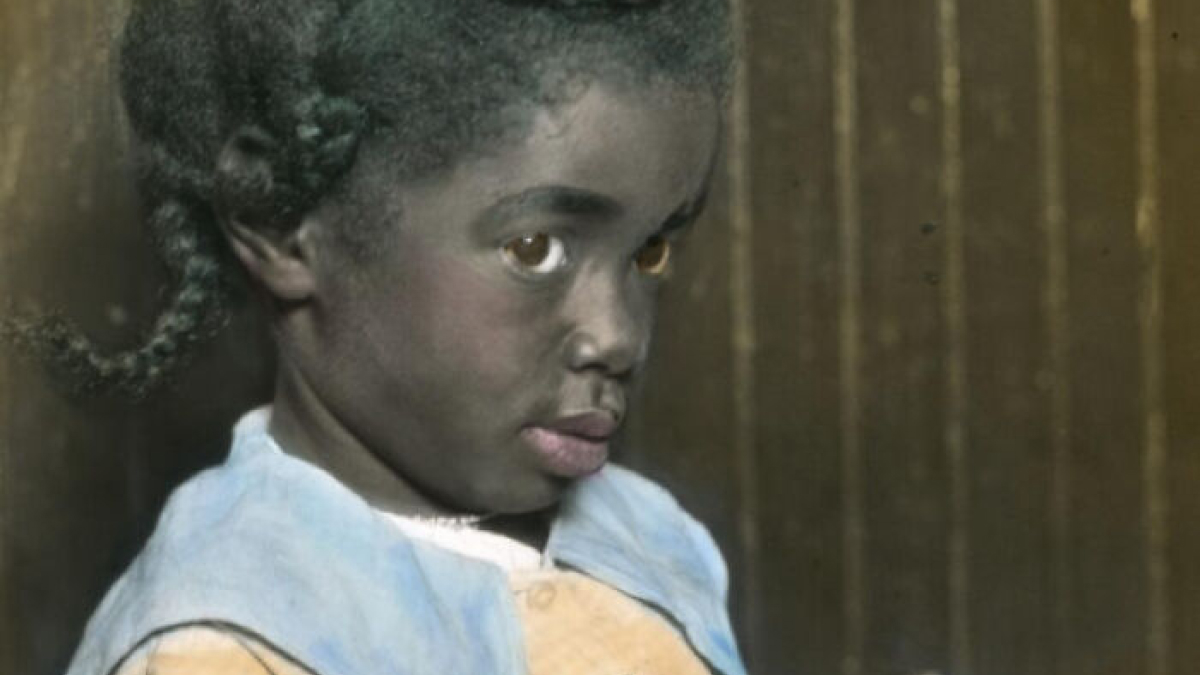 Young African American girl with braided hair in a colorized photo showing the reality of the 1920s.