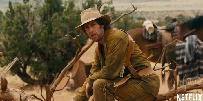 Actor in a western outfit sitting outdoors with horses and a tent behind, from a Netflix movies letdowns scene.