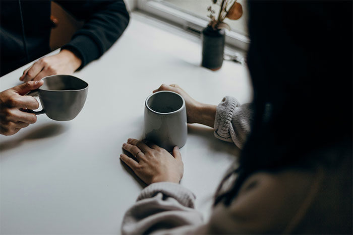 Couple sitting at a table with coffee mugs, tense atmosphere reflecting a woman angry after boyfriend dumped her.