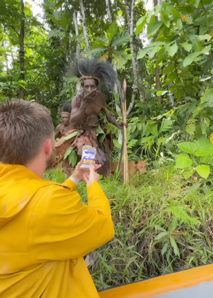 Influencer filming indigenous tribe member in traditional attire in a forest setting for viral TikTok stunt. Influencer filming indigenous tribe member in traditional attire in a forest setting for viral TikTok stunt.