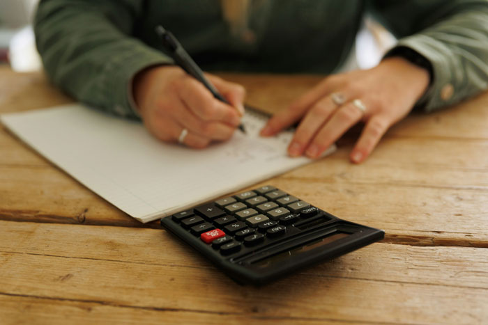 Person writing on paper with a calculator on a wooden table, symbolizing family demands for money conflict. Person writing on paper with a calculator on a wooden table, symbolizing family demands for money conflict.
