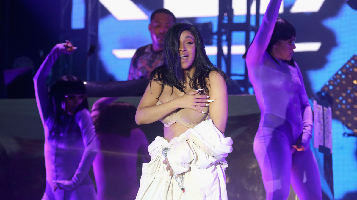 Female performer covering a wardrobe malfunction on stage during a concert with backup dancers in purple outfits.