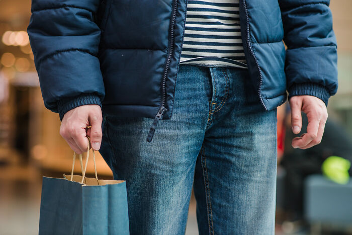 Person wearing a blue jacket and jeans holding a shopping bag, illustrating shopping a*******n and non-substance dependencies.