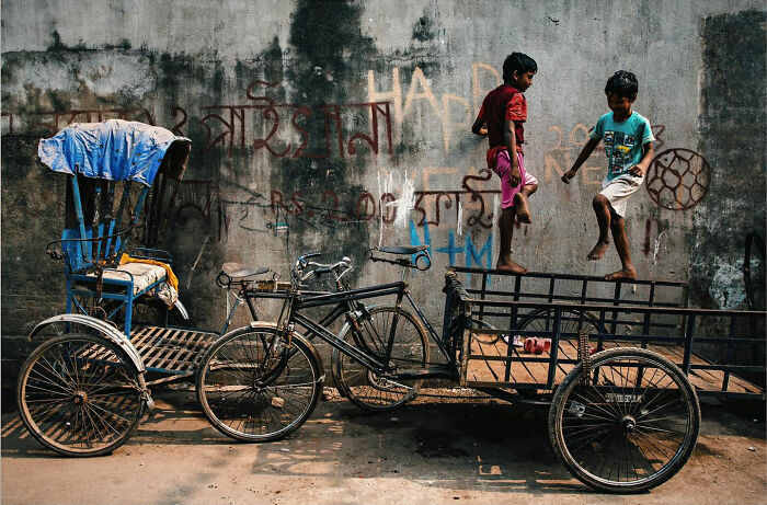 Two boys jump and play on a cart next to bikes in a candid everyday moment from Asia captured by photographer Gil Kreslavsky