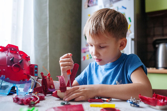 Young school kid focused on assembling a red mechanical toy, showcasing confidence while pulling off creative projects.