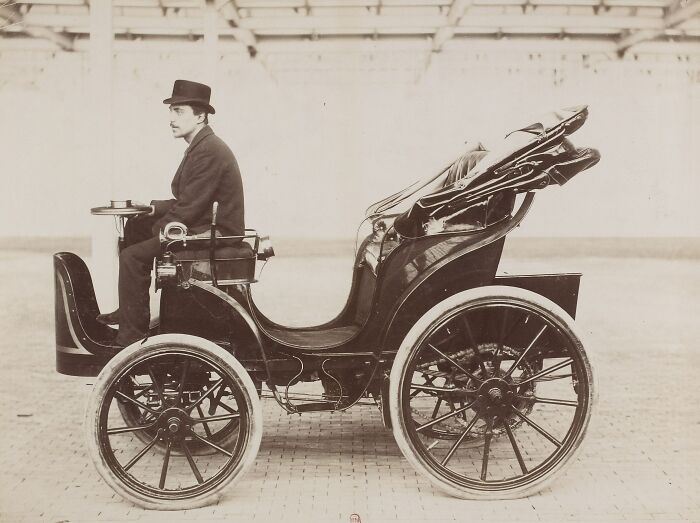 Man in vintage outfit sitting in one of the first cars from 100 years ago, showcasing how wild early automobiles were.