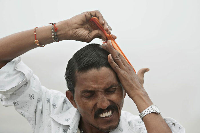 Man focused on grooming hair with orange comb in a candid everyday moment captured in Asia by photographer Gil Kreslavsky