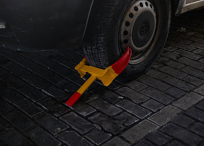 Car wheel locked with a boot device on dark pavement, representing jobs that only a person without a soul would do.