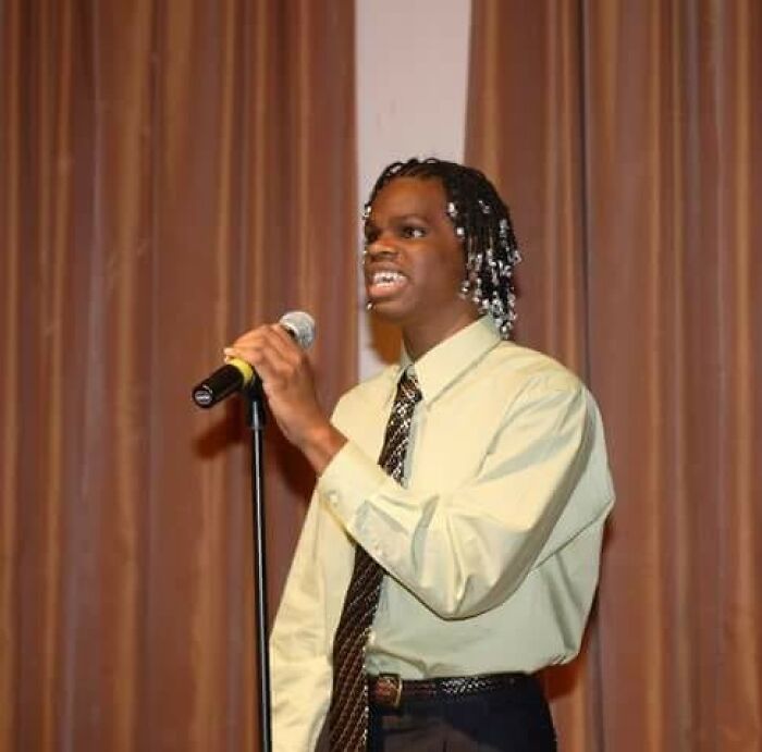 Young man with beaded hair speaking into a microphone on stage, showcasing proof that superhumans walk among us.
