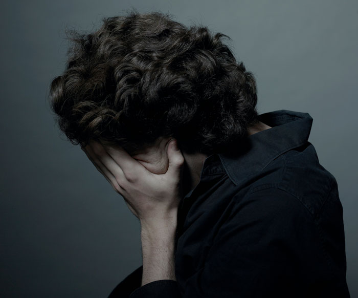 Teen boy covering face with hands, feeling distressed and regretful in a dimly lit setting representing loss and hardship. Teen boy covering face with hands, feeling distressed and regretful in a dimly lit setting representing loss and hardship.