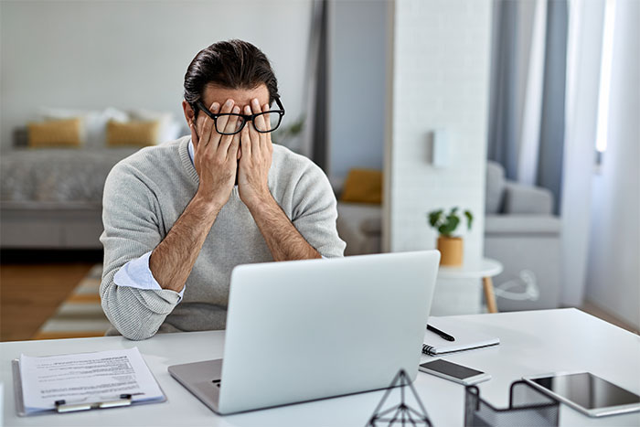 Man sitting at desk covering face in frustration after learning wife’s family secretly cyber-bullied him online. Man sitting at desk covering face in frustration after learning wife’s family secretly cyber-bullied him online.