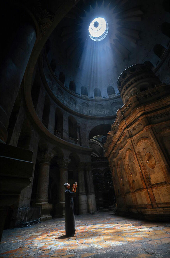 Man praying inside ancient temple with light beams shining down, a candid everyday moment from Asia captured by photographer.