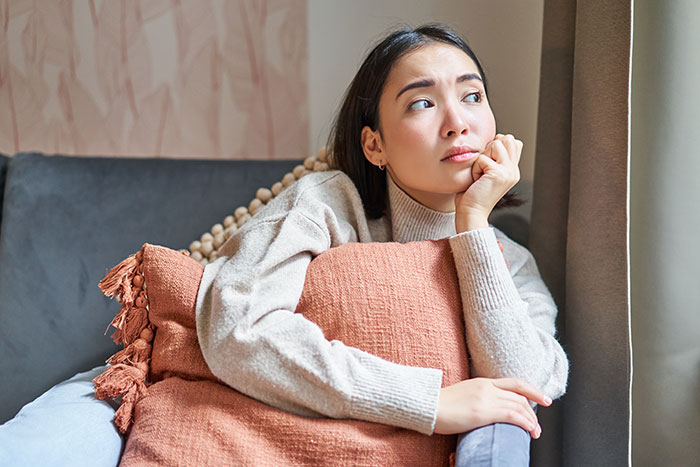 Woman looking worried on couch, hugging a cushion, showing signs of jealousy and panic in a home setting. Woman looking worried on couch, hugging a cushion, showing signs of jealousy and panic in a home setting.