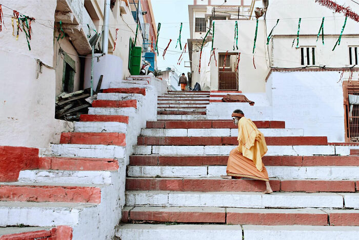 Man in traditional clothing climbing red and white stairs, a candid everyday moment from Asia captured by photographer Gil Kreslavsky.