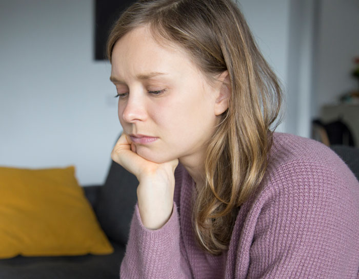 Sad woman in a purple sweater sitting indoors, reflecting on family demands and strained relationships over money. Sad woman in a purple sweater sitting indoors, reflecting on family demands and strained relationships over money.
