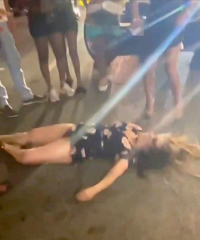 Woman lying unconscious on the ground after being punched during a violent Cincinnati brawl, surrounded by bystanders. Woman lying unconscious on the ground after being punched during a violent Cincinnati brawl, surrounded by bystanders.