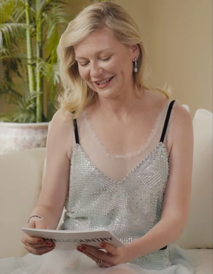 Kirsten Dunst smiling and looking down while holding a magazine, revealing the real pronunciation of her name. Kirsten Dunst smiling and looking down while holding a magazine, revealing the real pronunciation of her name.