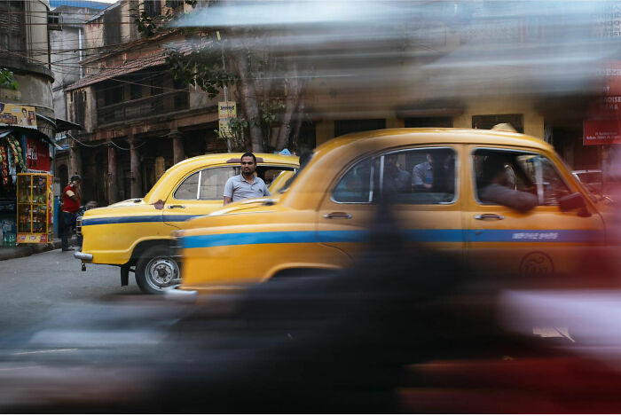 Yellow taxis and a man on a busy street in Asia, capturing candid everyday moments by photographer Gil Kreslavsky.