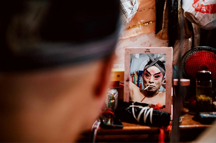 Person applying traditional makeup seen through a mirror in a candid everyday moment from Asia captured by photographer Gil Kreslavsky
