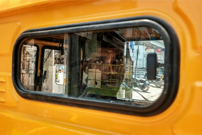 Reflection of a busy Asian street scene in the window of a yellow vehicle, capturing candid everyday moments.