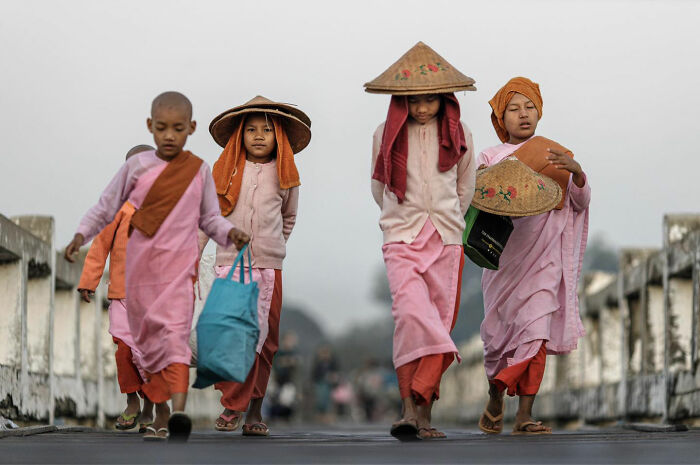 Young Asian girls in traditional attire walking on a bridge, capturing candid everyday moments in Asia by photographer Gil Kreslavsky