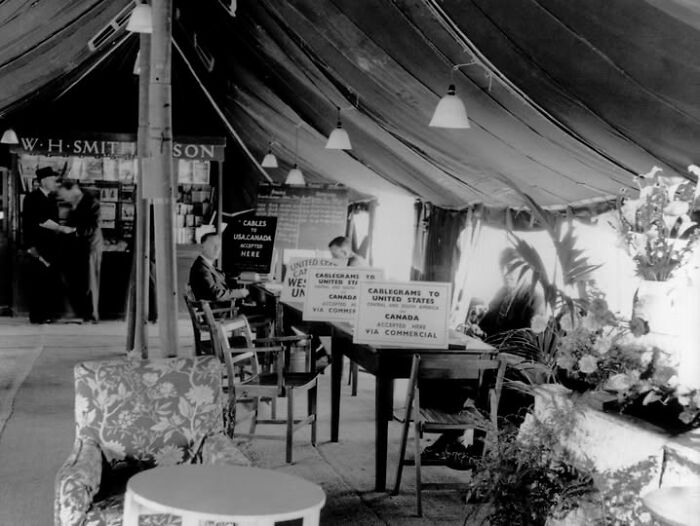 Vintage black and white image of a glamorous flying lounge with seating, plants, and telegraph service signs.