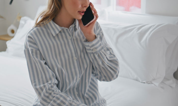 Young woman in striped shirt sitting on bed, talking on phone, dealing with family demands for money conflict. Young woman in striped shirt sitting on bed, talking on phone, dealing with family demands for money conflict.