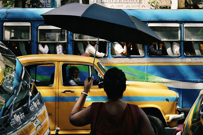 Woman holding black umbrella among colorful vehicles, capturing candid everyday moments from Asia by photographer Gil Kreslavsky.