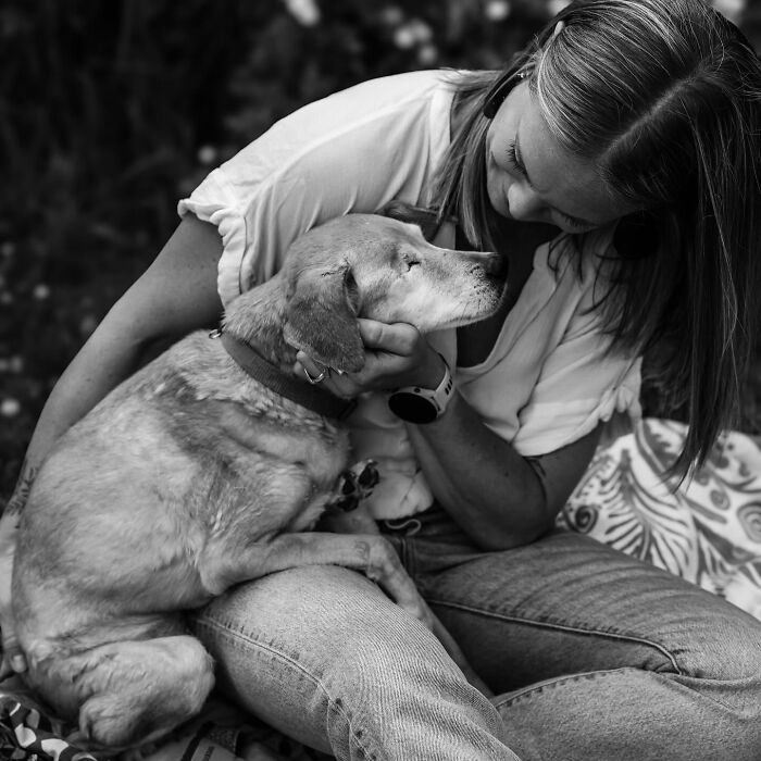 Woman gently holding and comforting one-eyed dog, capturing touching final moments between pets and their humans in black and white.