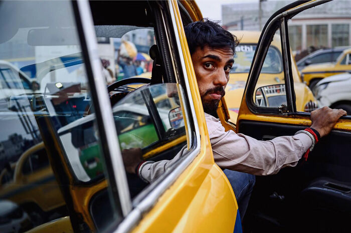 Man captured in candid everyday moment stepping out of a yellow taxi in a busy Asian city street by photographer Gil Kreslavsky.