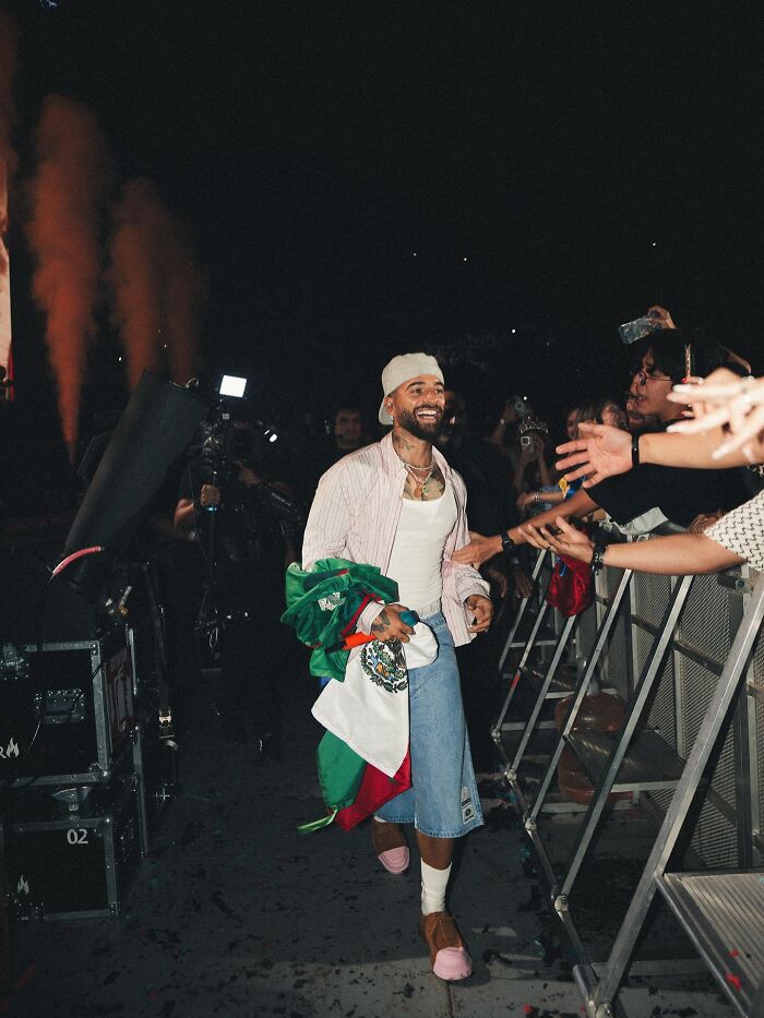Singer holding a Mexican flag, smiling and walking backstage while fans reach out during a concert moment that sparked debate online. Singer holding a Mexican flag, smiling and walking backstage while fans reach out during a concert moment that sparked debate online.