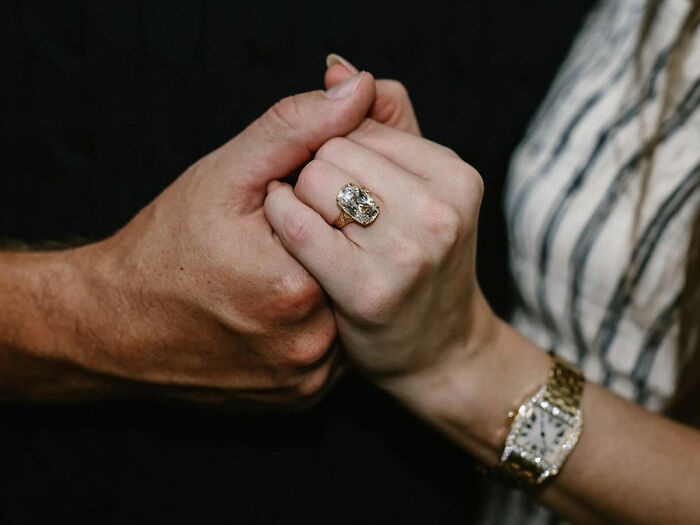 Close-up of two hands clasped together, one wearing a large ring and a gold watch, symbolizing engagement and relationship. Close-up of two hands clasped together, one wearing a large ring and a gold watch, symbolizing engagement and relationship.
